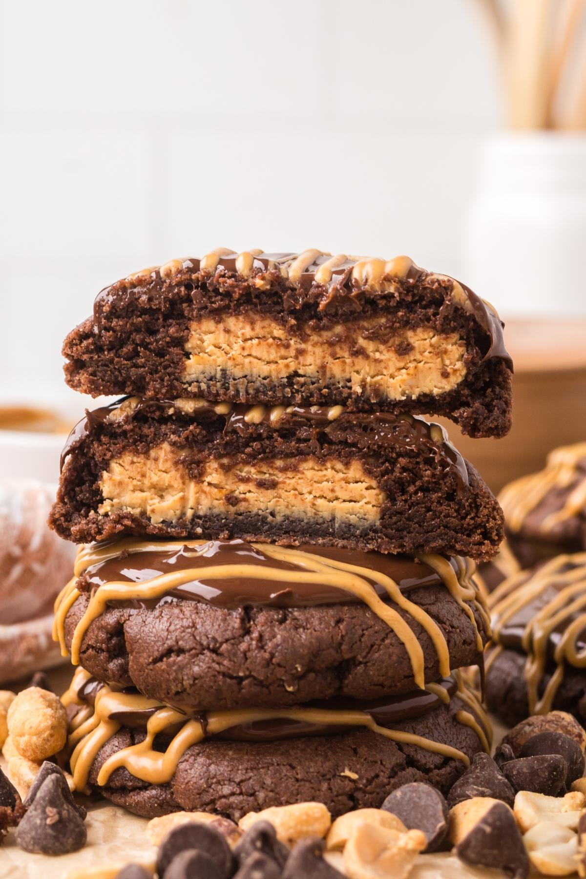 Stack of chocolate peanut butter cookies, some halved to show peanut butter filling, drizzled with chocolate.
