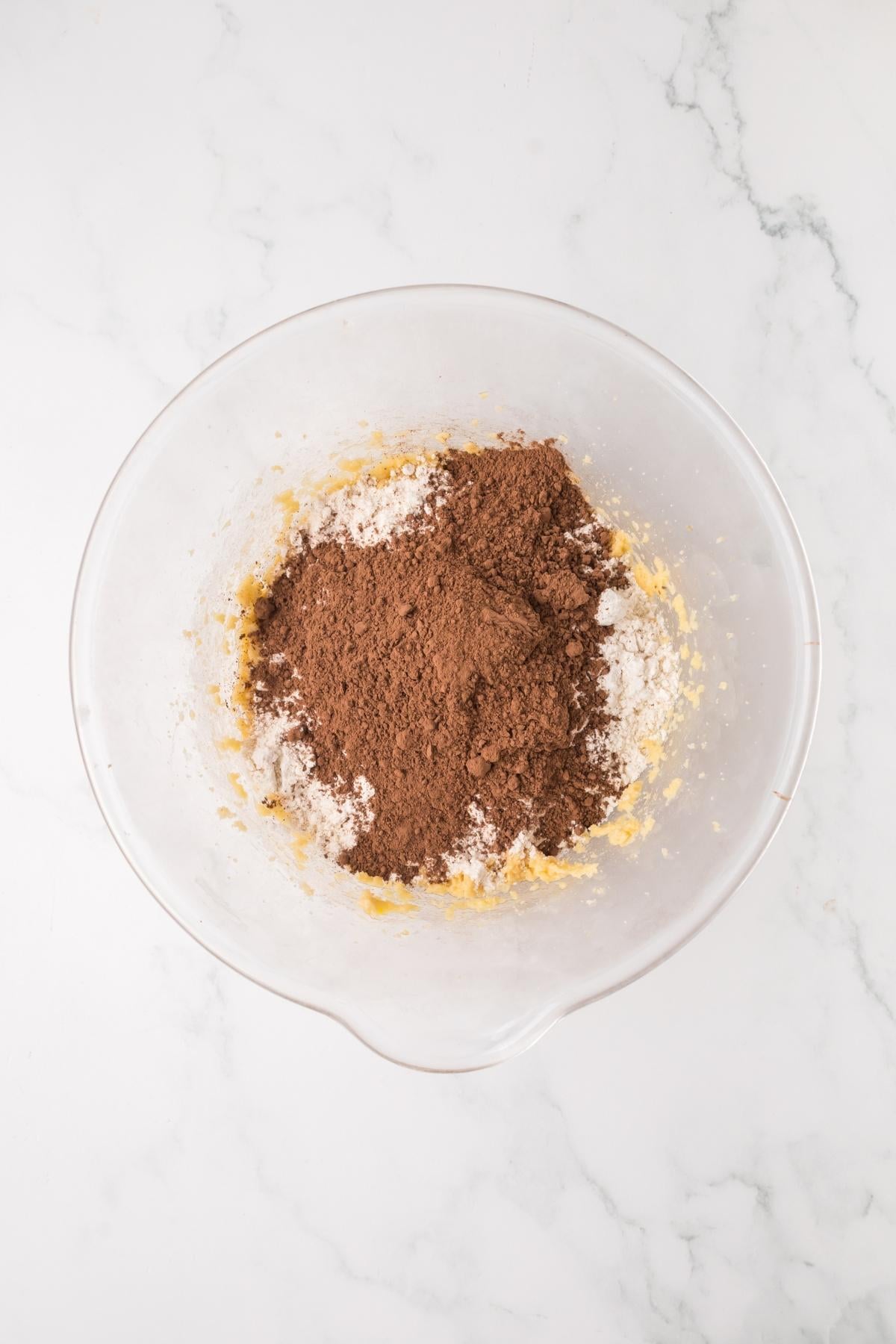 A mixing bowl with cocoa powder, flour, and sugar on a marble countertop.