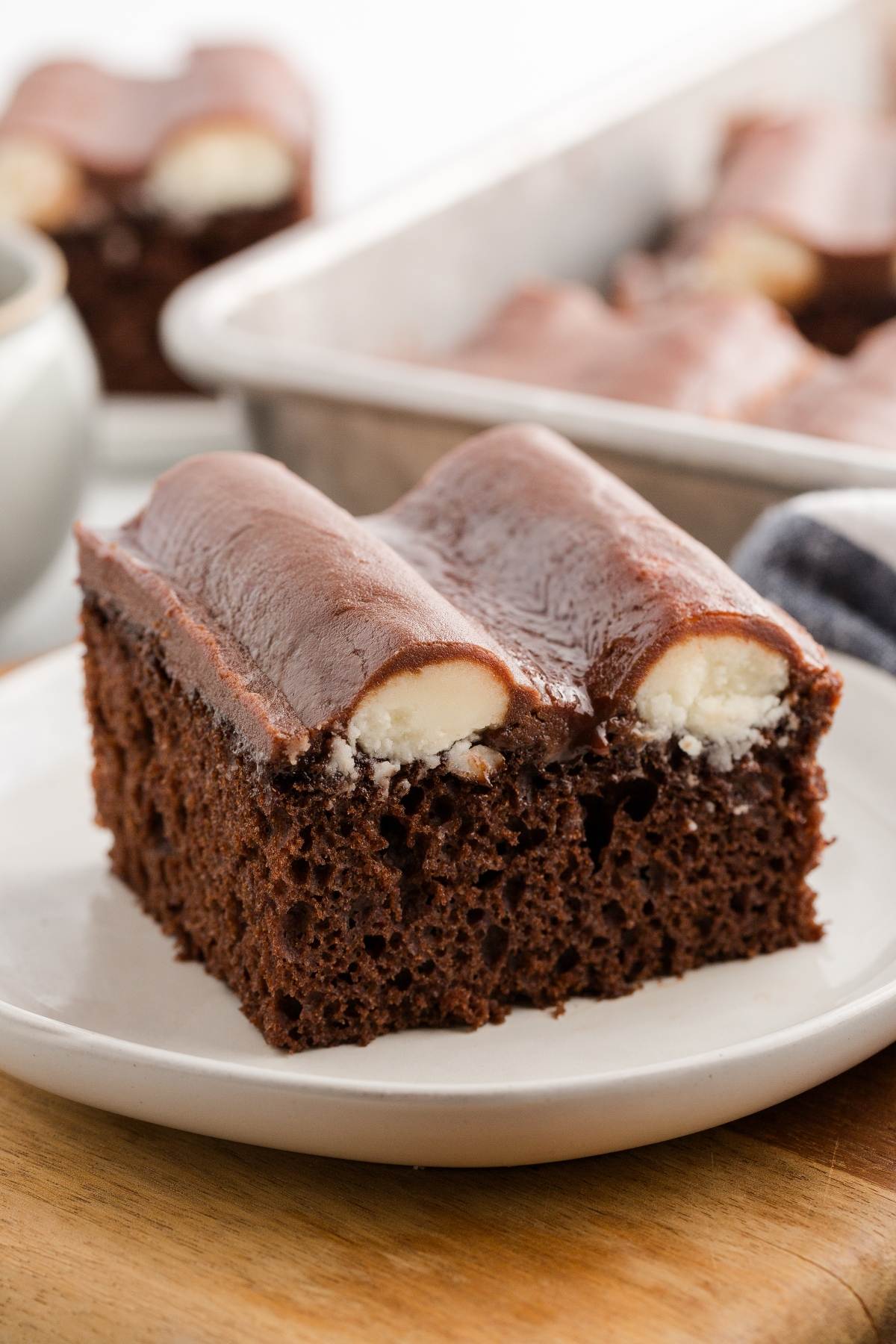 A slice of chocolate cake topped with two chocolate-covered cream-filled rolls on a white plate.