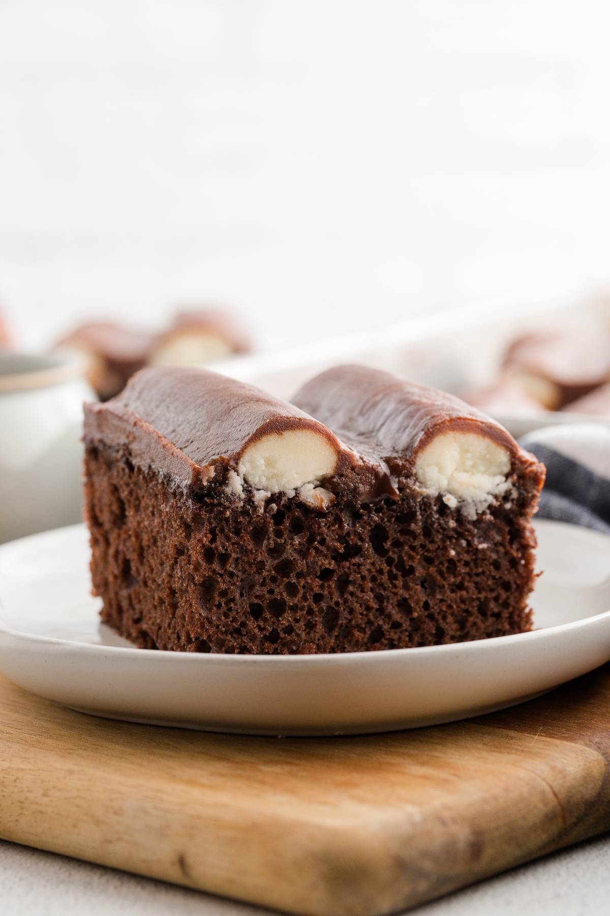 Two slices of chocolate cake with cream filling on a white plate, resting on a wooden board.