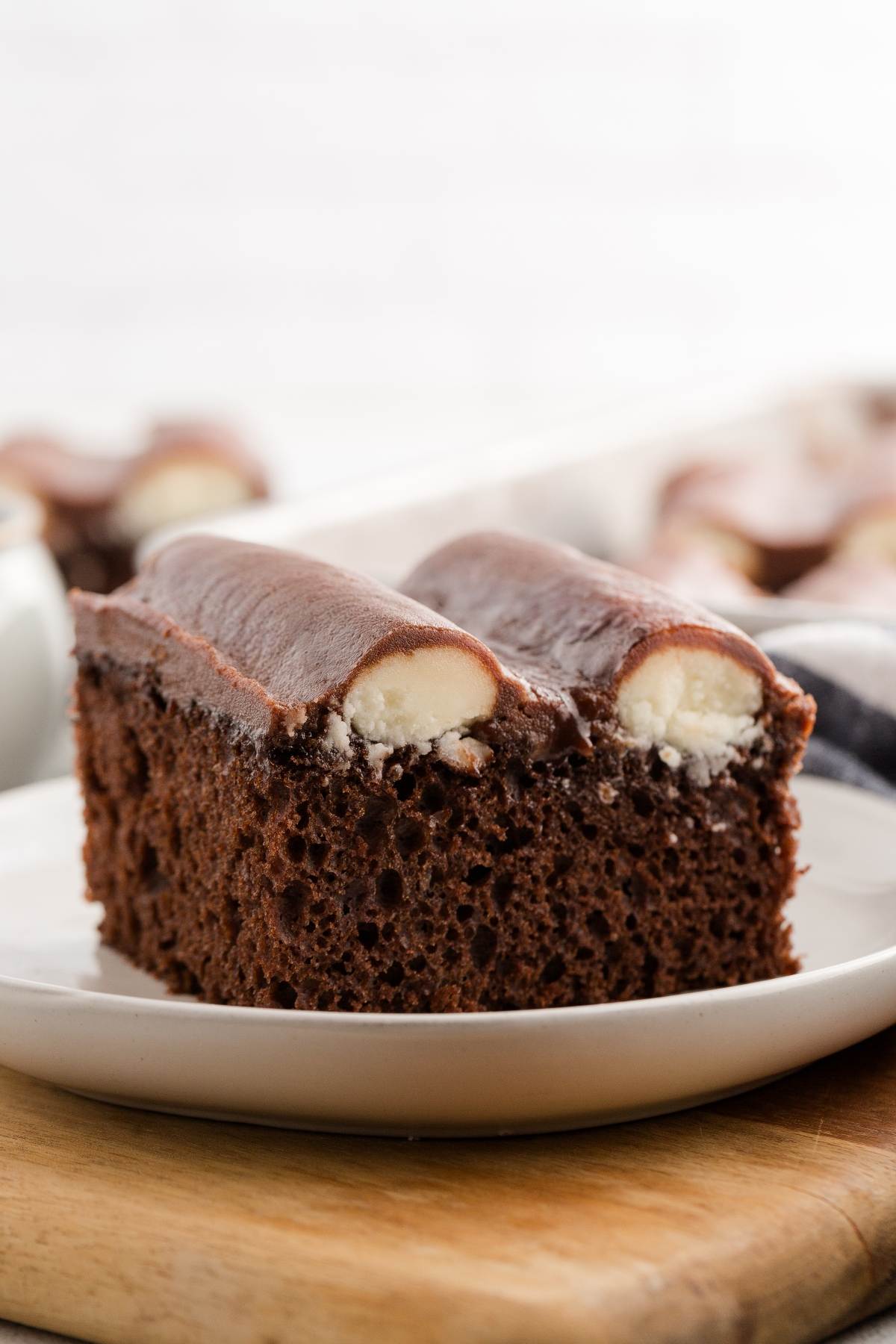 A slice of chocolate cake with two filled chocolate rolls on top, served on a white plate.