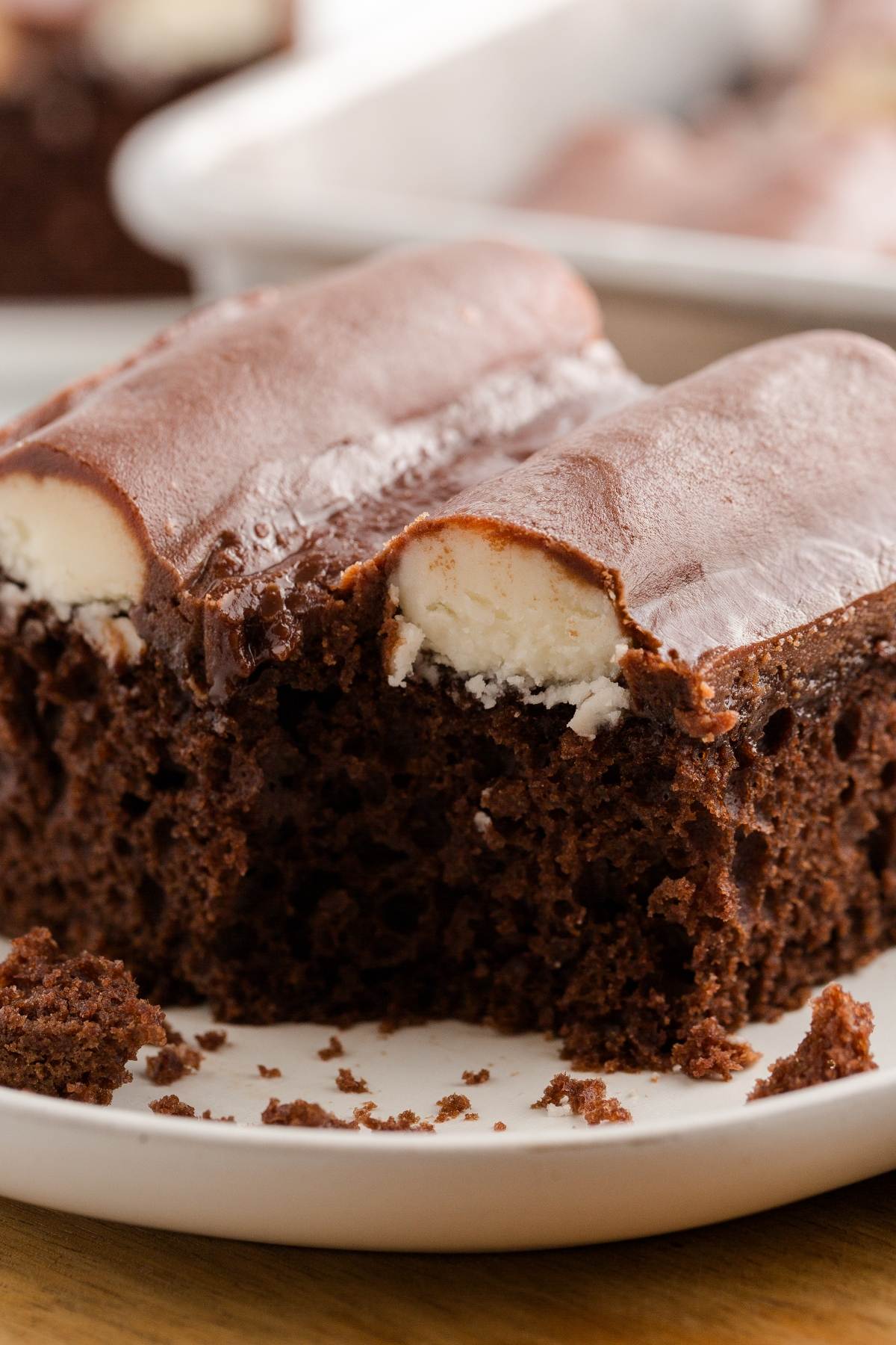 A close-up of a chocolate cake slice with creamy filling and chocolate frosting on a white plate.
