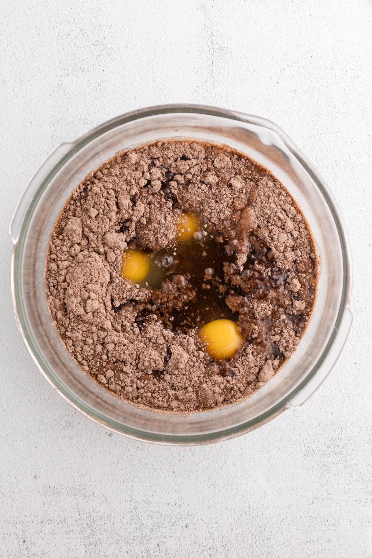A glass bowl with brownie mix, eggs, and liquid ingredients before mixing.