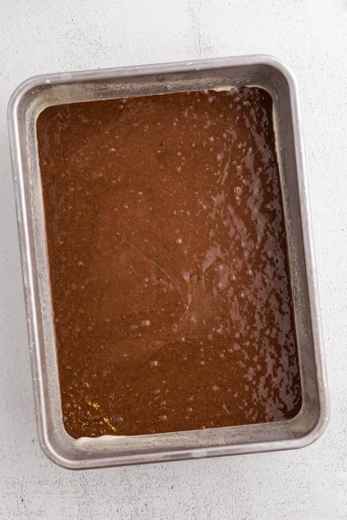 A metal baking pan filled with chocolate cake batter on a light-colored surface.