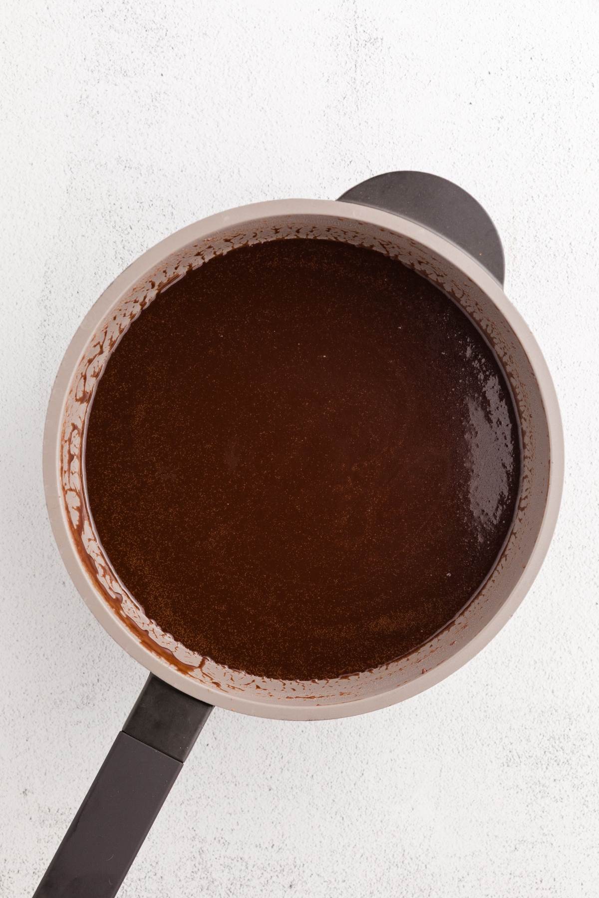 A saucepan filled with a smooth, glossy chocolate mixture on a white surface.