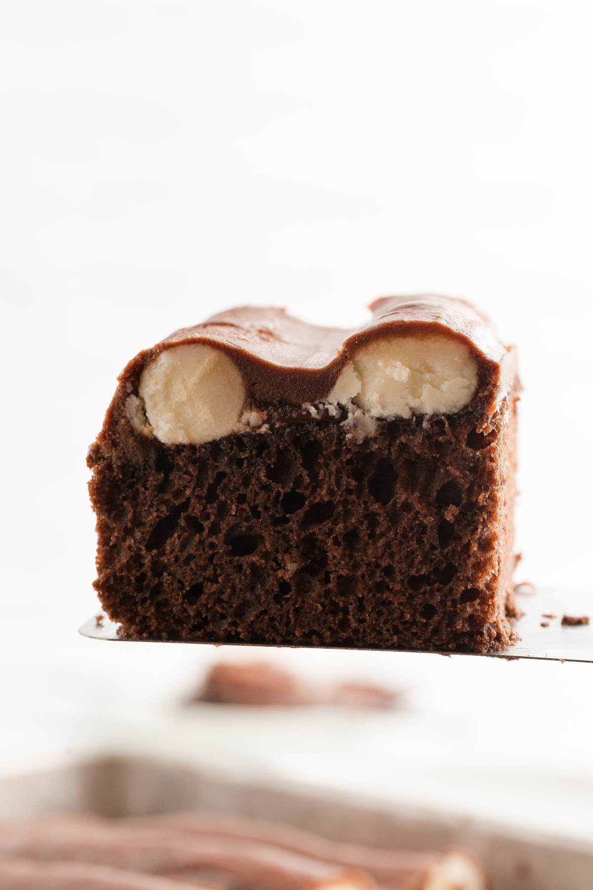 A close-up of a slice of  bumpy chocolate cake with a chocolate glaze and visible banana slices inside.