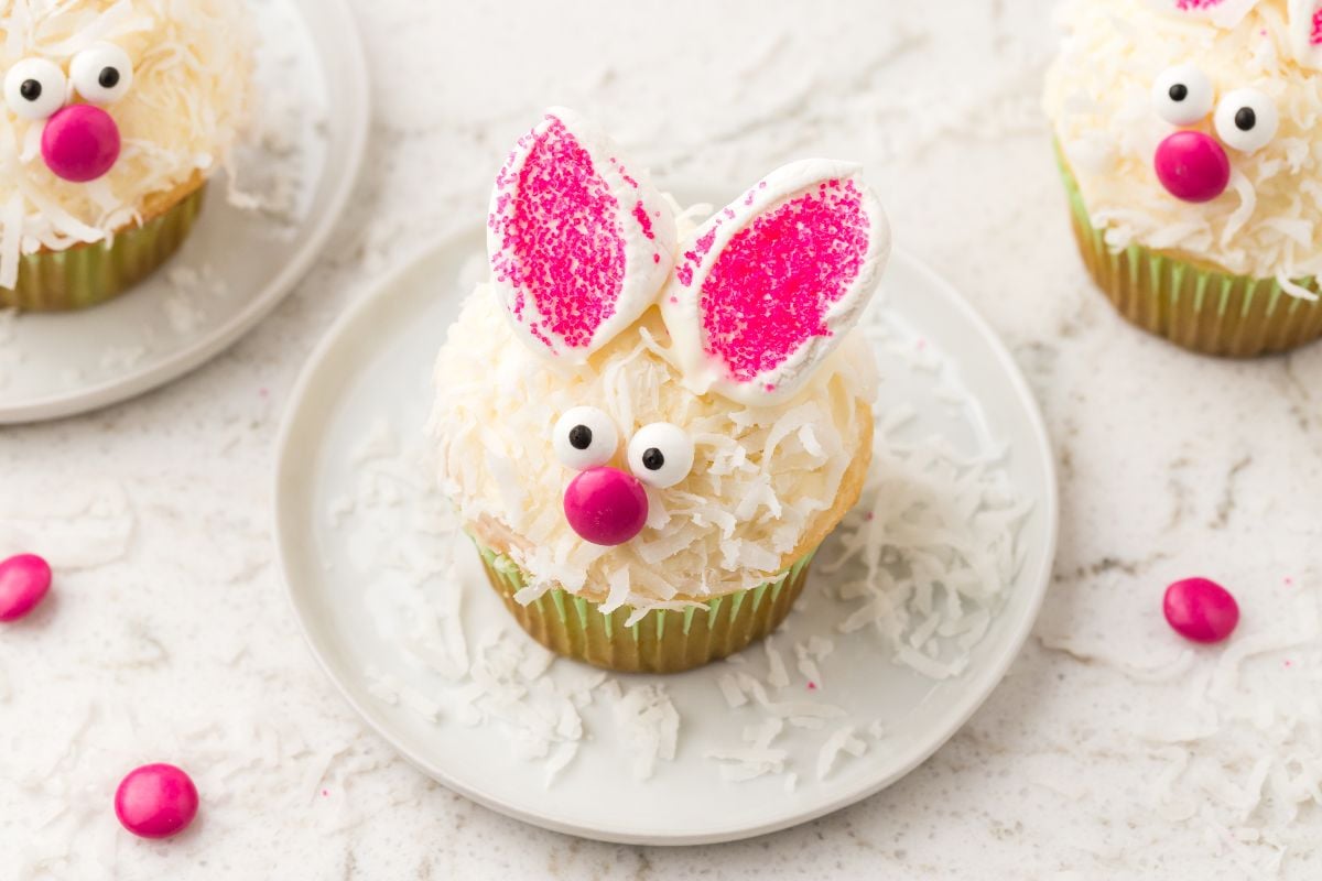 A bunny cupcake with pink ears, candy eyes, and a pink nose sits on a white plate&mdash;one of the cutest bunny cupcakes you&rsquo;ll ever see.