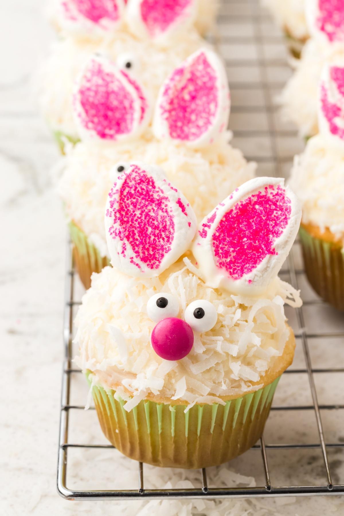 Cupcake decorated as a bunny with marshmallow ears, pink nose, candy eyes, and shredded coconut fur.
