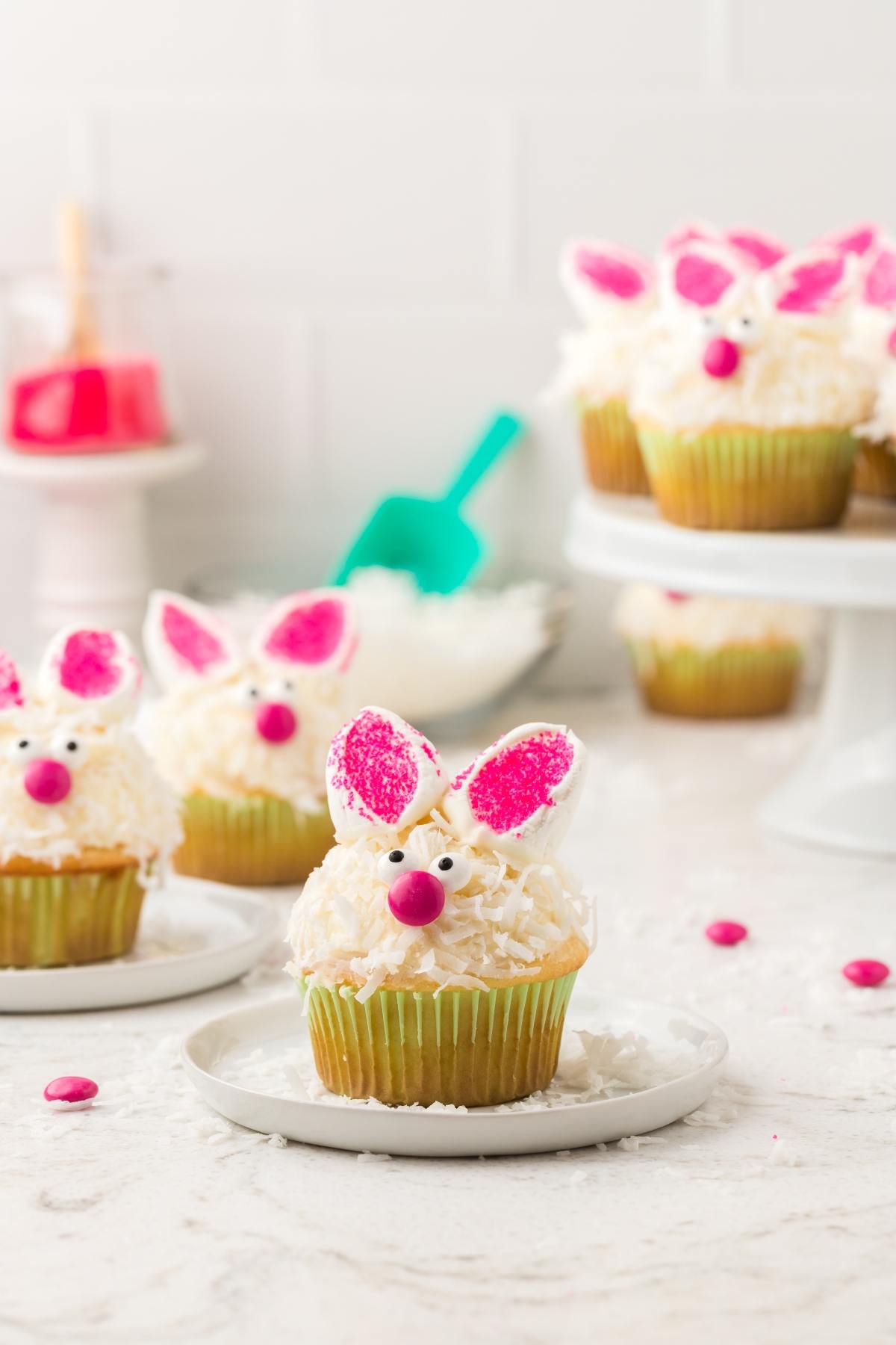Cupcakes decorated as bunnies with pink ears and noses, displayed on plates and a cake stand.