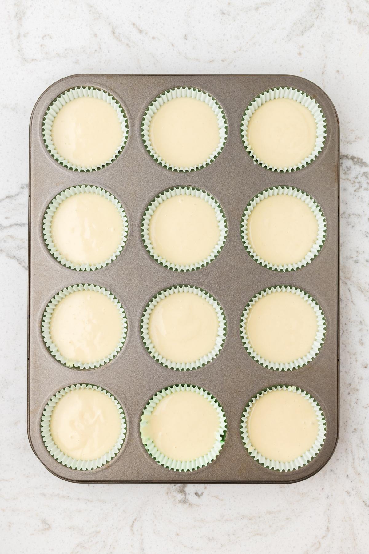 A muffin pan with 12 paper liners filled with cupcake batter, ready to be baked.