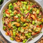 A vibrant Cashew Crunch Edamame Salad featuring edamame, cabbage, carrots, cashews, cilantro, and sesame seeds served in a white bowl.