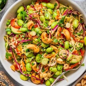 A vibrant Cashew Crunch Edamame Salad featuring edamame, cabbage, carrots, cashews, cilantro, and sesame seeds served in a white bowl.