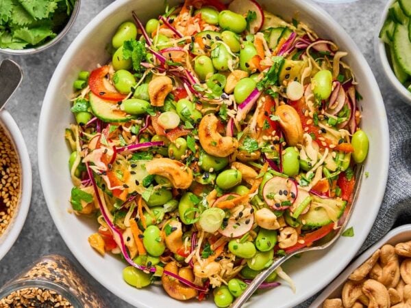 A vibrant Cashew Crunch Edamame Salad featuring edamame, cabbage, carrots, cashews, cilantro, and sesame seeds served in a white bowl.
