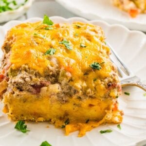 A slice of cheesy Cattle Drive Casserole topped with parsley sits on a white plate with a fork.