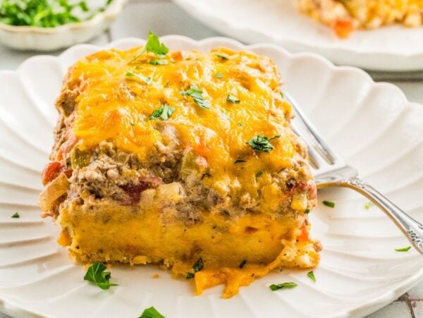 A slice of cheesy Cattle Drive Casserole topped with parsley sits on a white plate with a fork.