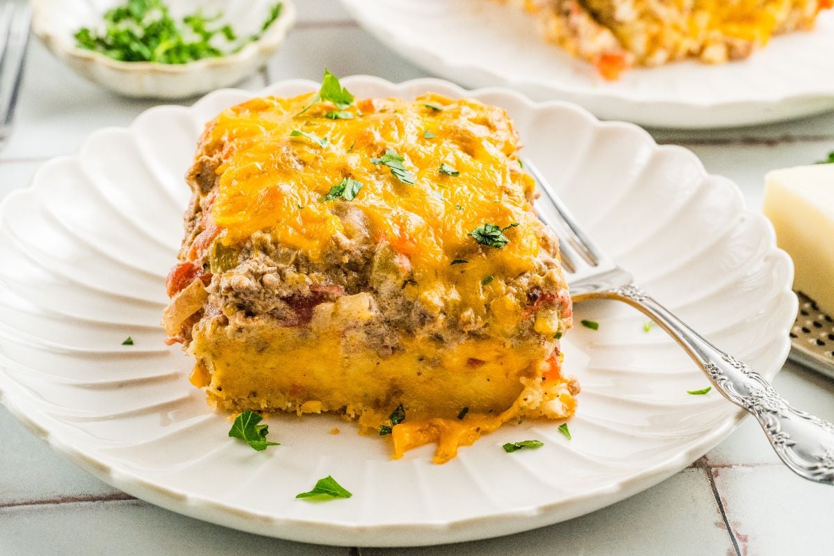 A slice of cheesy Cattle Drive Casserole topped with parsley on a white plate with a fork.