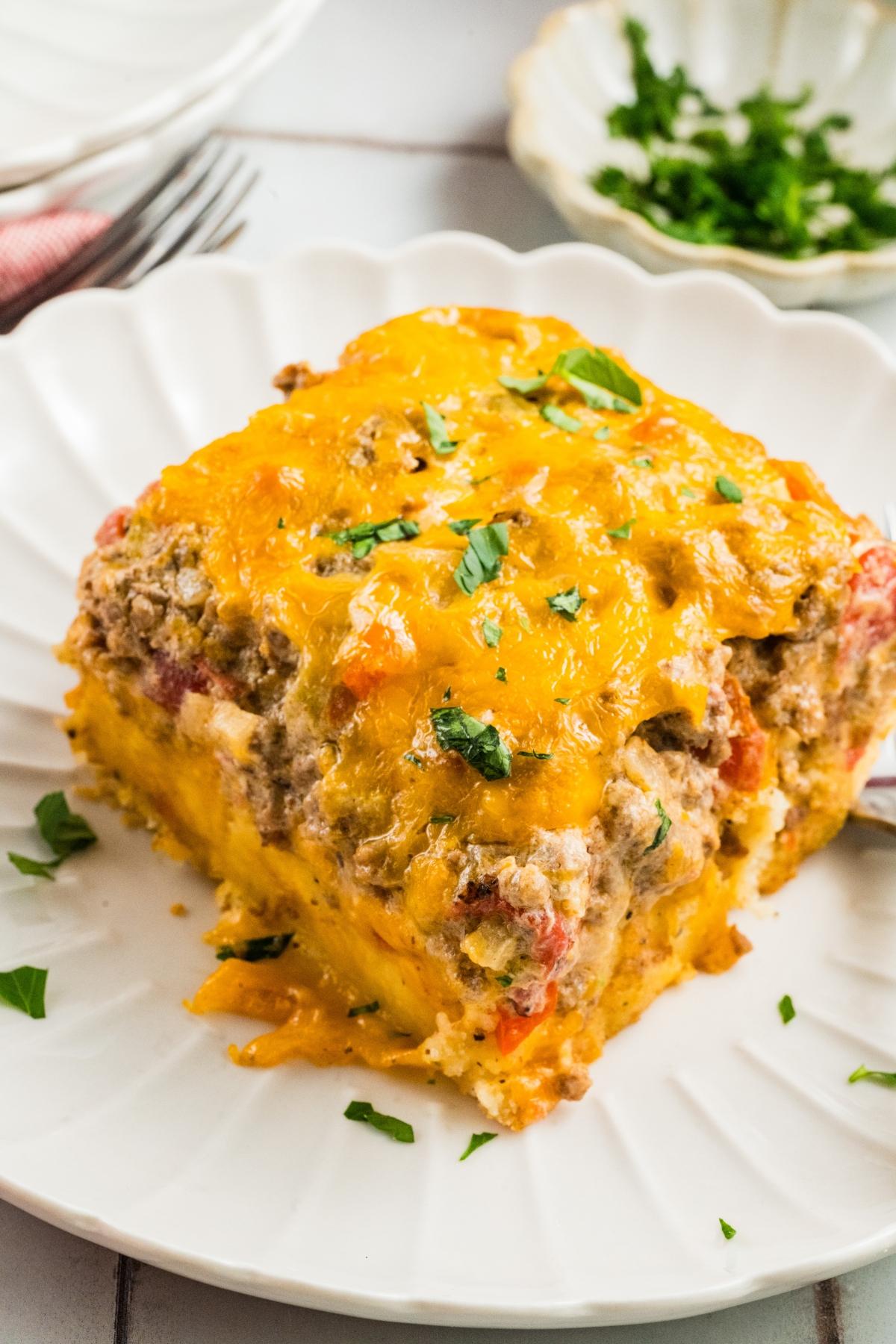A slice of cheesy casserole with ground meat, tomatoes, and herbs on a white plate.