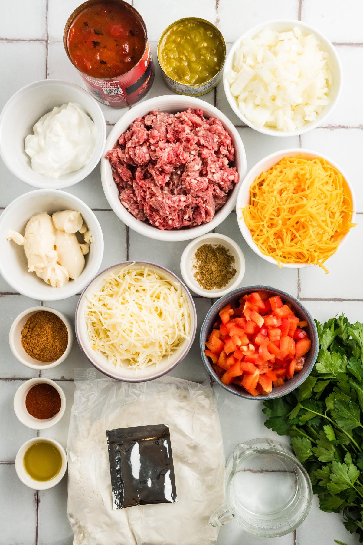 Various taco casserole ingredients in bowls, including ground beef, cheese, tomatoes, onions, and seasonings.