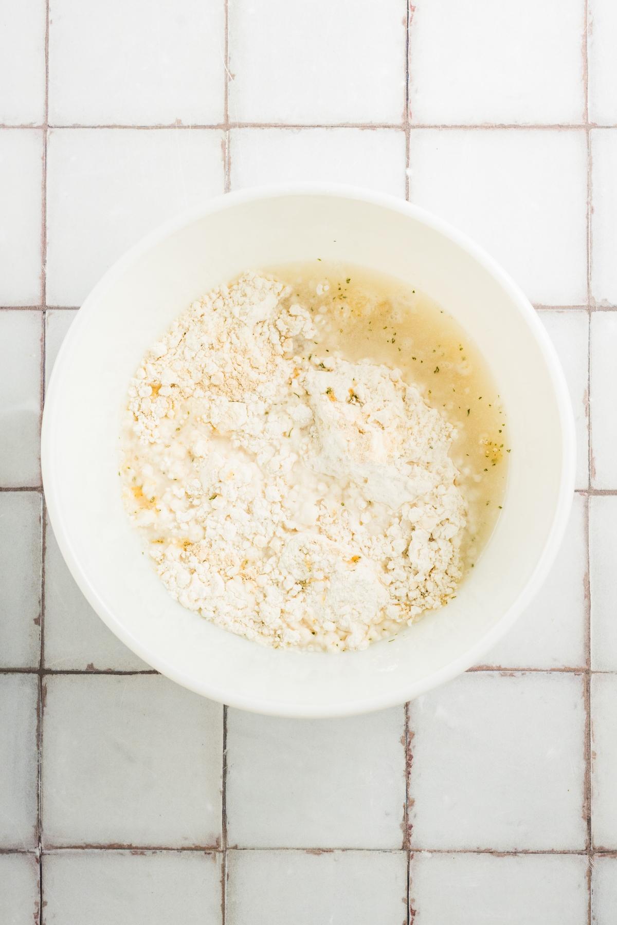 White bowl with flour and water mixture on a tiled countertop, viewed from above.