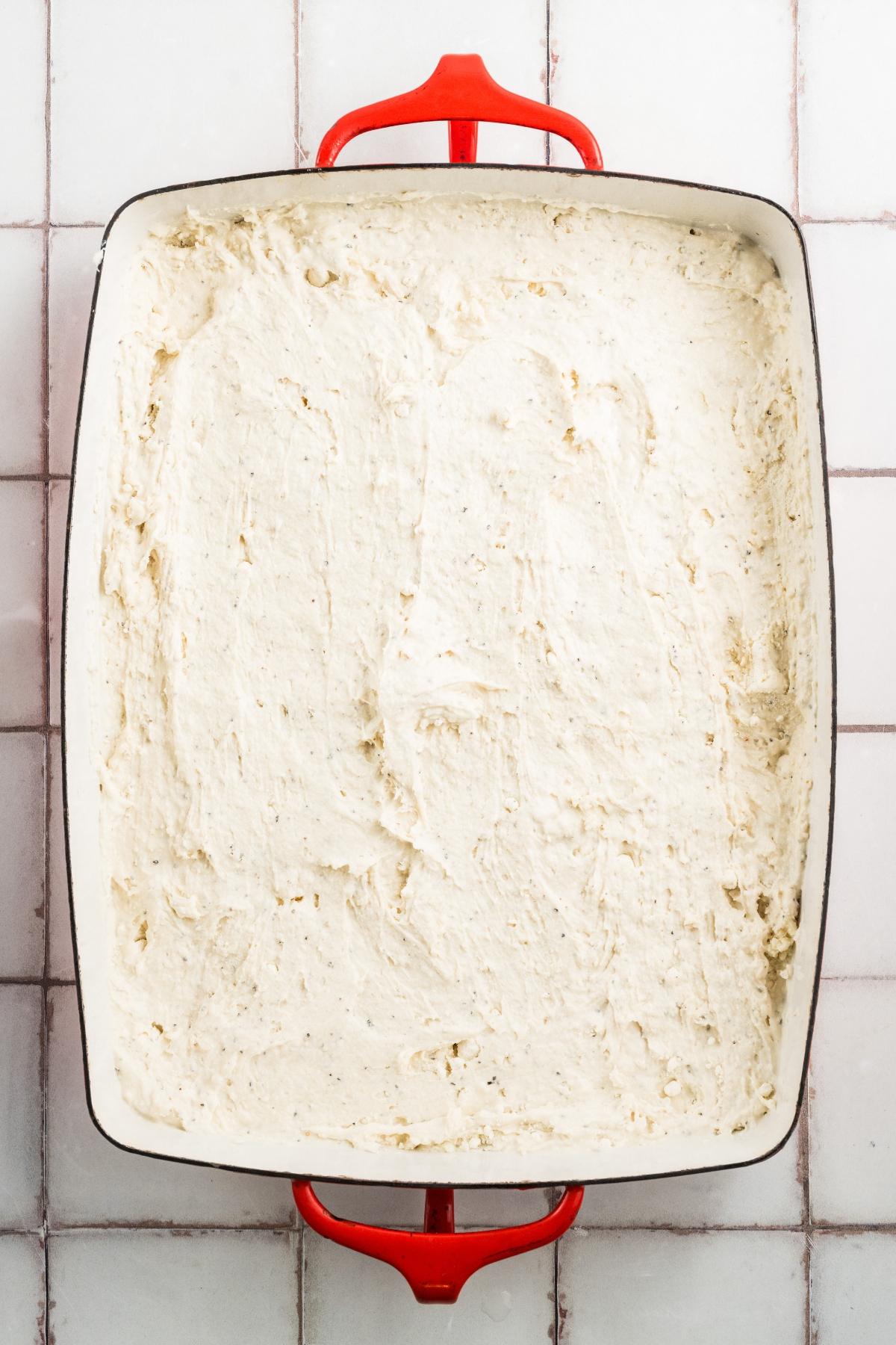 A rectangular pan with red handles filled with an even layer of unbaked cake batter.