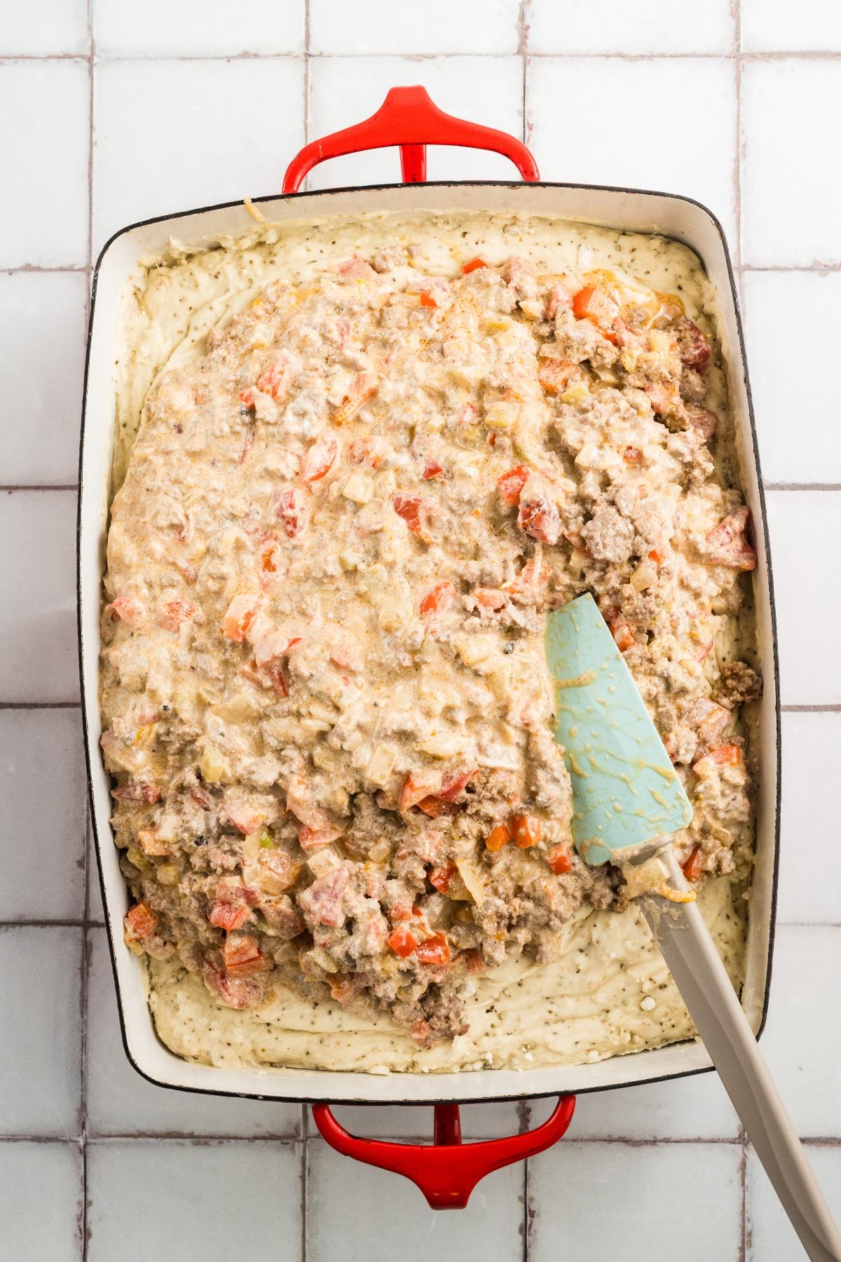 A baking dish with an unbaked casserole mixture of ground meat, chopped vegetables, and creamy sauce.