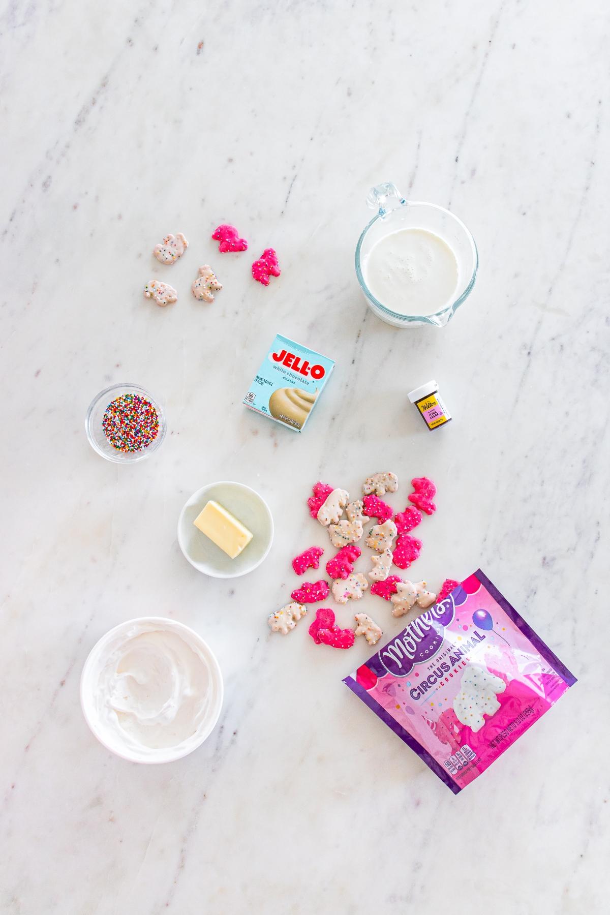 Ingredients for funfetti treats on a marble surface, including marshmallows, butter, sprinkles, and cream.