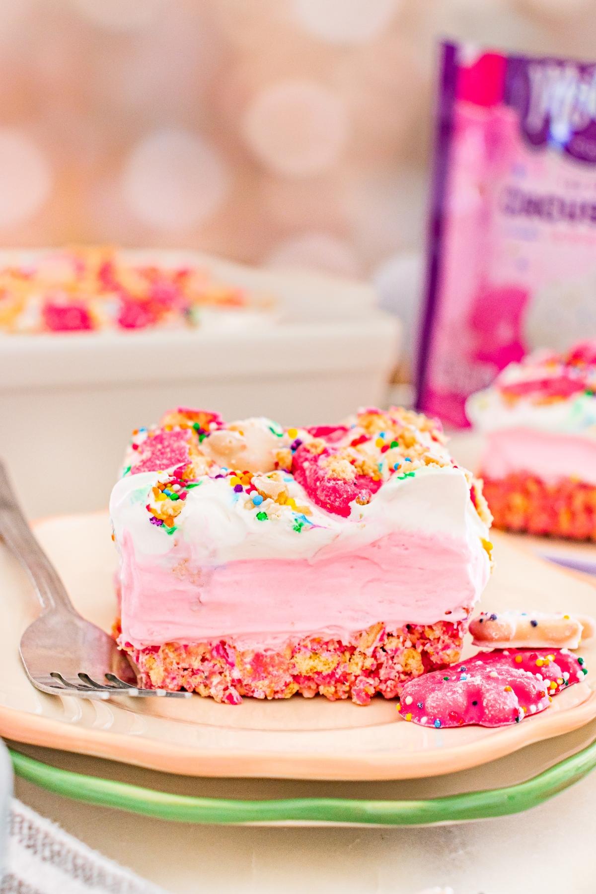 A colorful dessert bar with pink layers, sprinkles, and animal cookies on a plate with a fork.