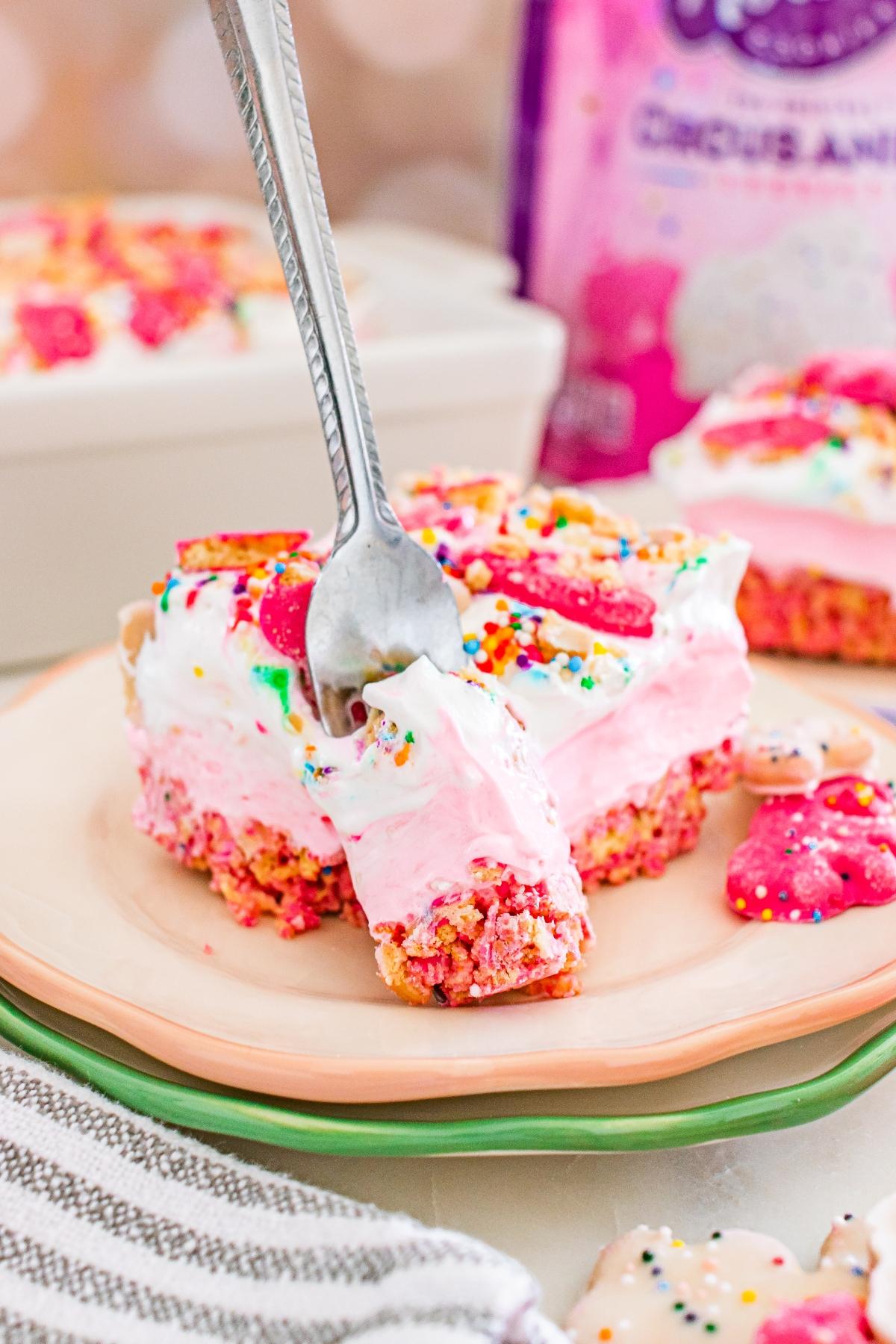 A fork digs into a pink and white frosted dessert bar topped with sprinkles and animal cookies.