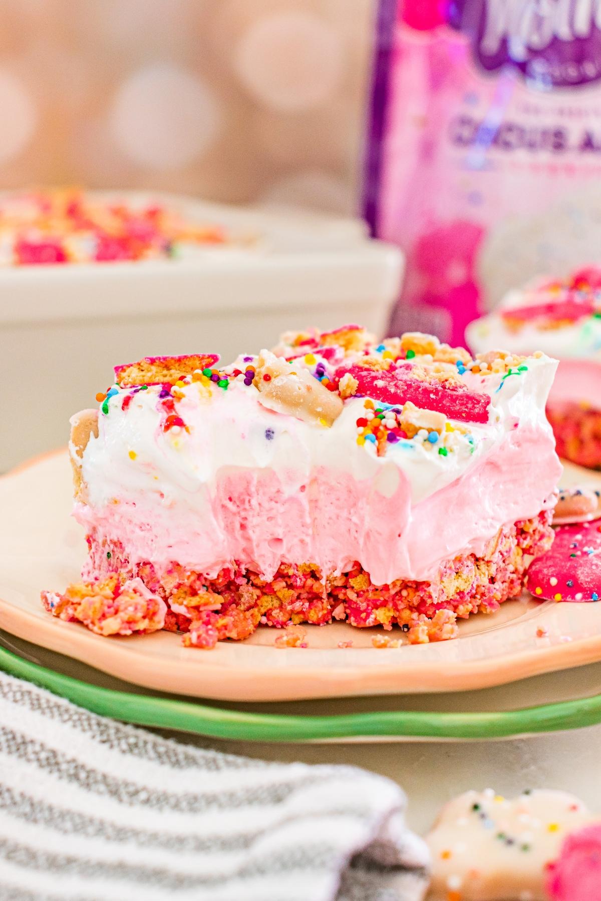 A slice of pink and white layered dessert topped with colorful sprinkles and cookies on a plate.