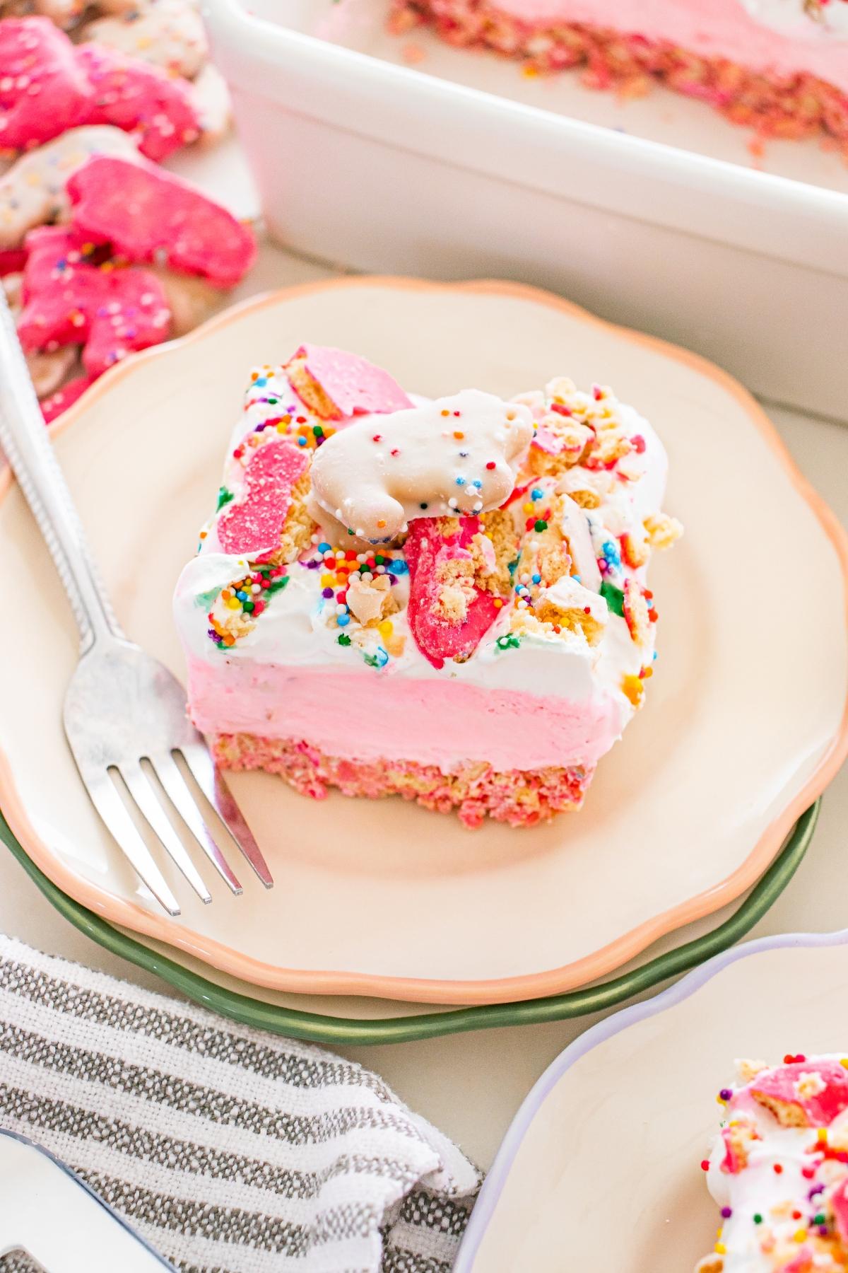 A slice of frosted animal cookie ice cream cake topped with colorful sprinkles and animal cookies on a plate.