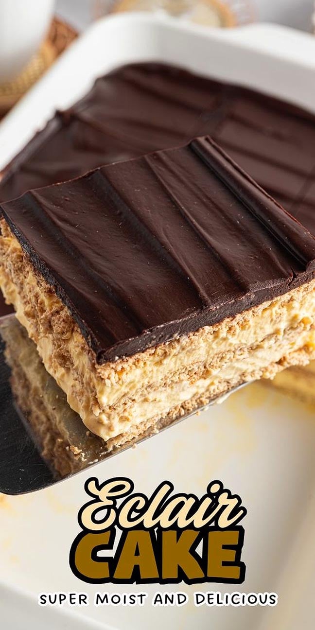 A slice of chocolate-topped Eclair Cake with creamy layers is being served from a white dish.