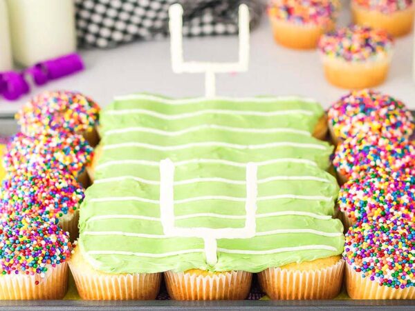 Football stadium cupcakes decorated as a football field with green icing and rainbow-sprinkle "fans" on the sides.