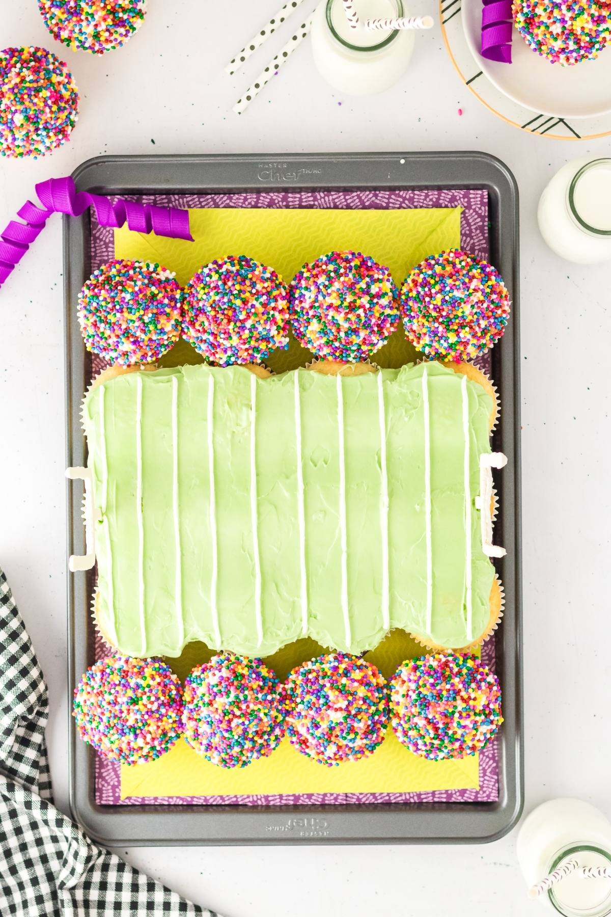 Football stadium cupcakes arranged as a football field, with green frosting and colorful sprinkles on a baking tray.
