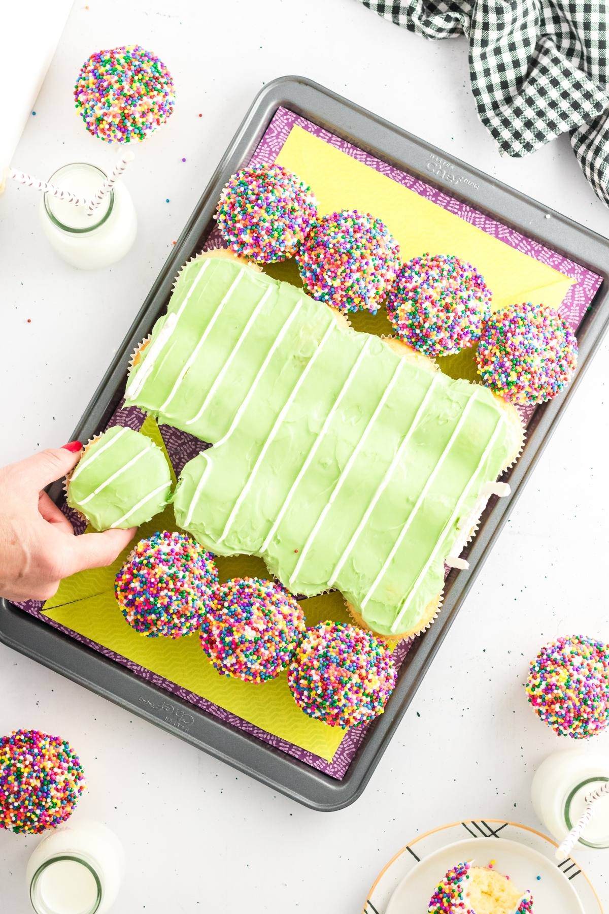 A tray with a pull apart cupcake cake and colorful sprinkle cupcakes, with a hand taking a cupcake.