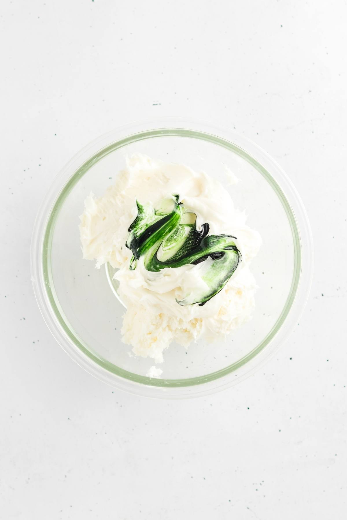 A glass bowl with white creamy mixture and streaks of green food coloring on top.