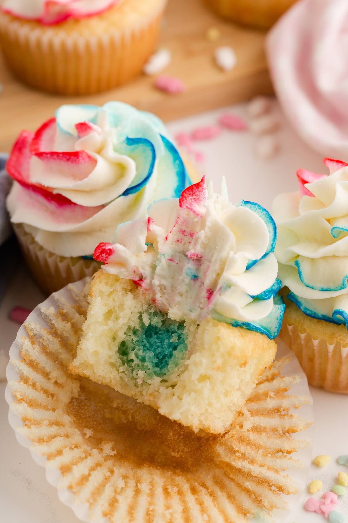 A Gender reveal  cupcake with red, white, and blue frosting and a blue filling inside, shown with a bite taken out.