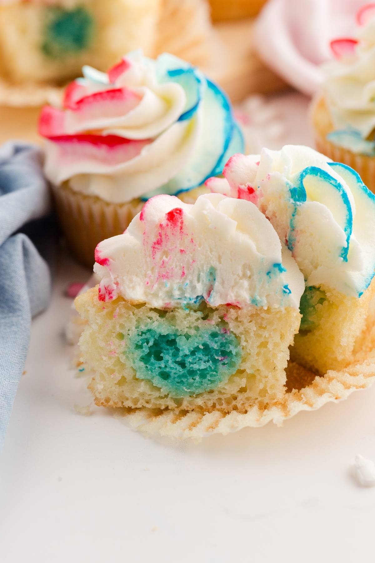A Gender reveal  cupcake with red, white, and blue frosting, cut in half to reveal a blue filling inside.