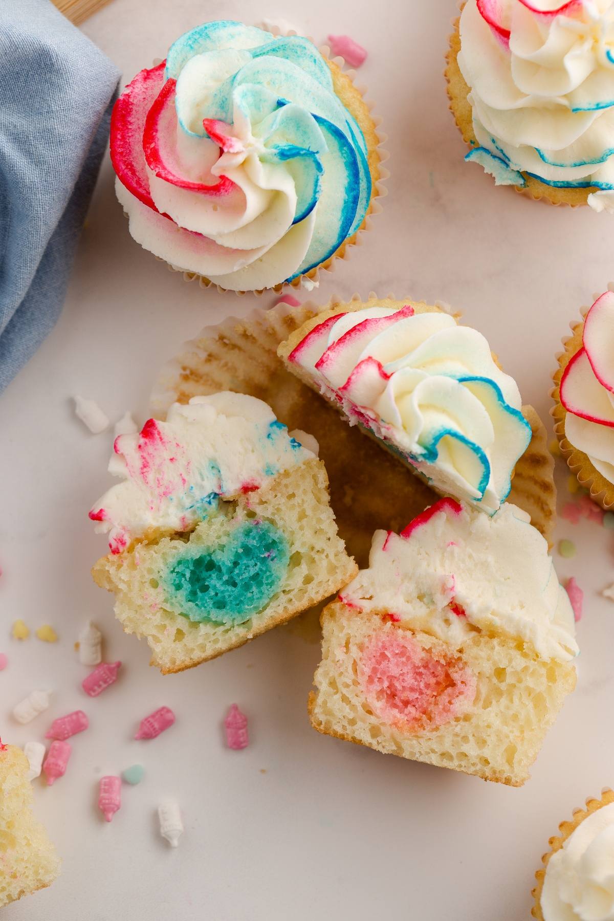 Gender reveal cupcake with colorful red, blue, and white frosting, cut open to reveal a vibrant red and blue center.