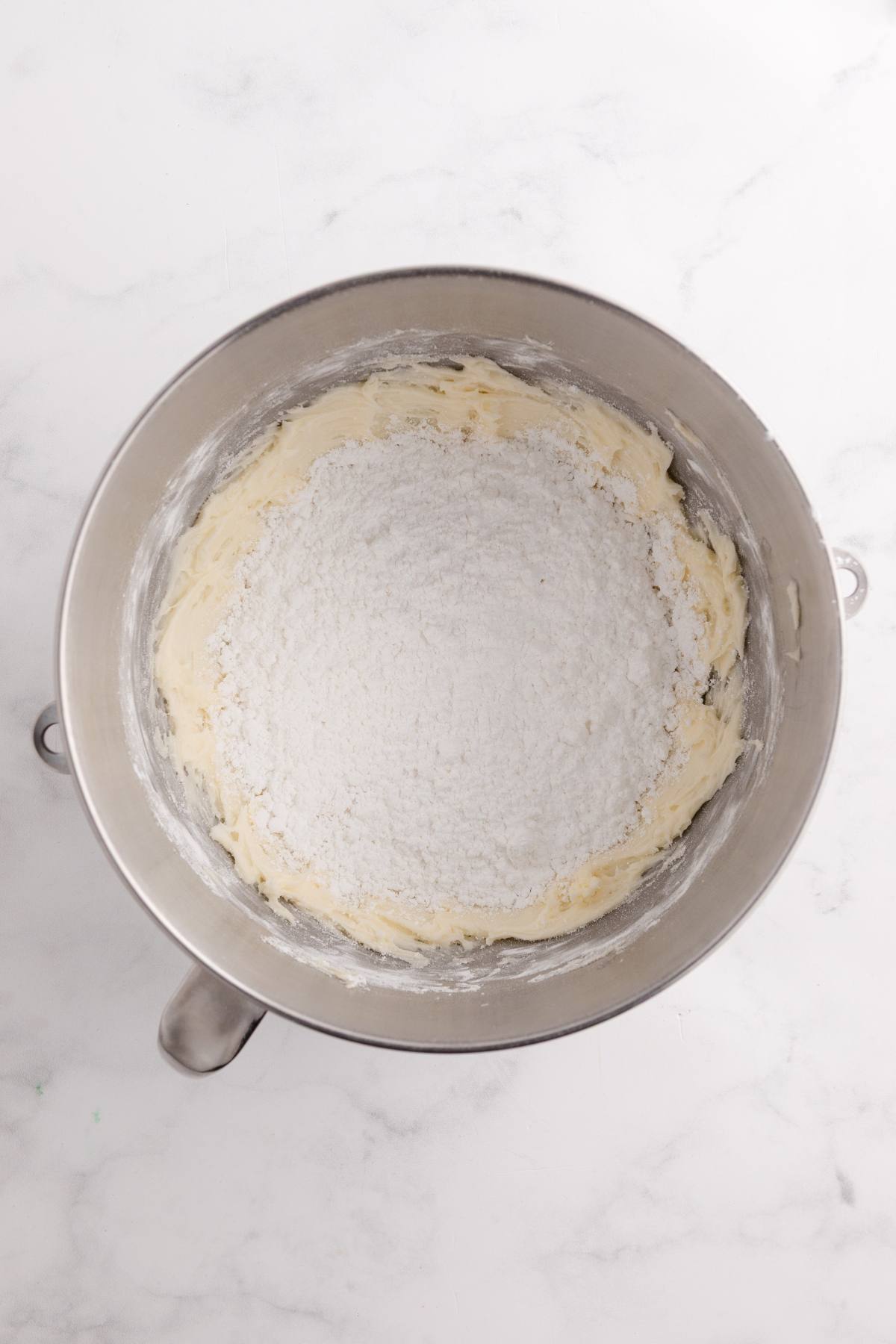 A mixing bowl with flour on top of creamed butter and sugar, ready to be mixed for baking.