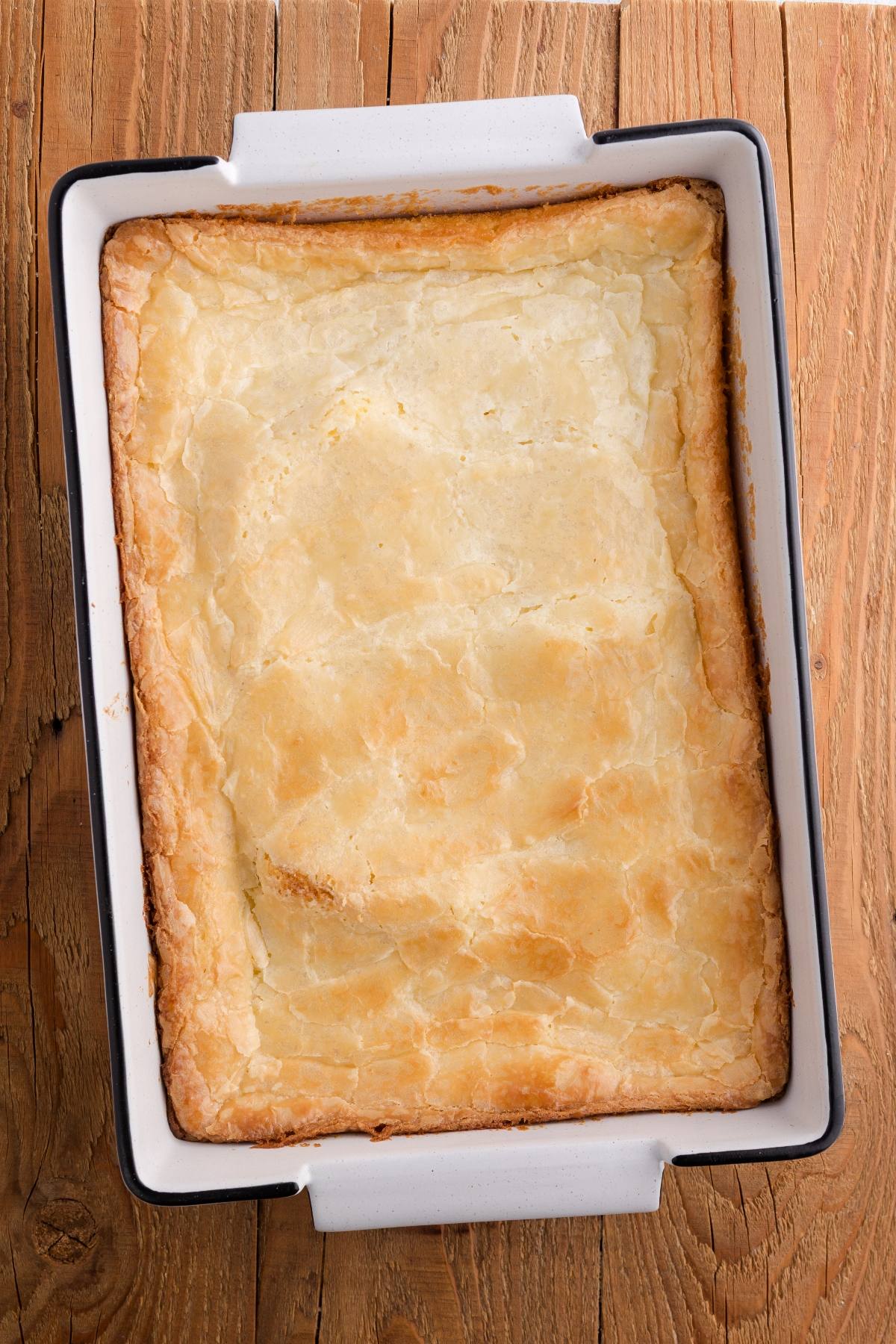A golden, flaky puff pastry baked in a rectangular white dish on a wooden surface.
