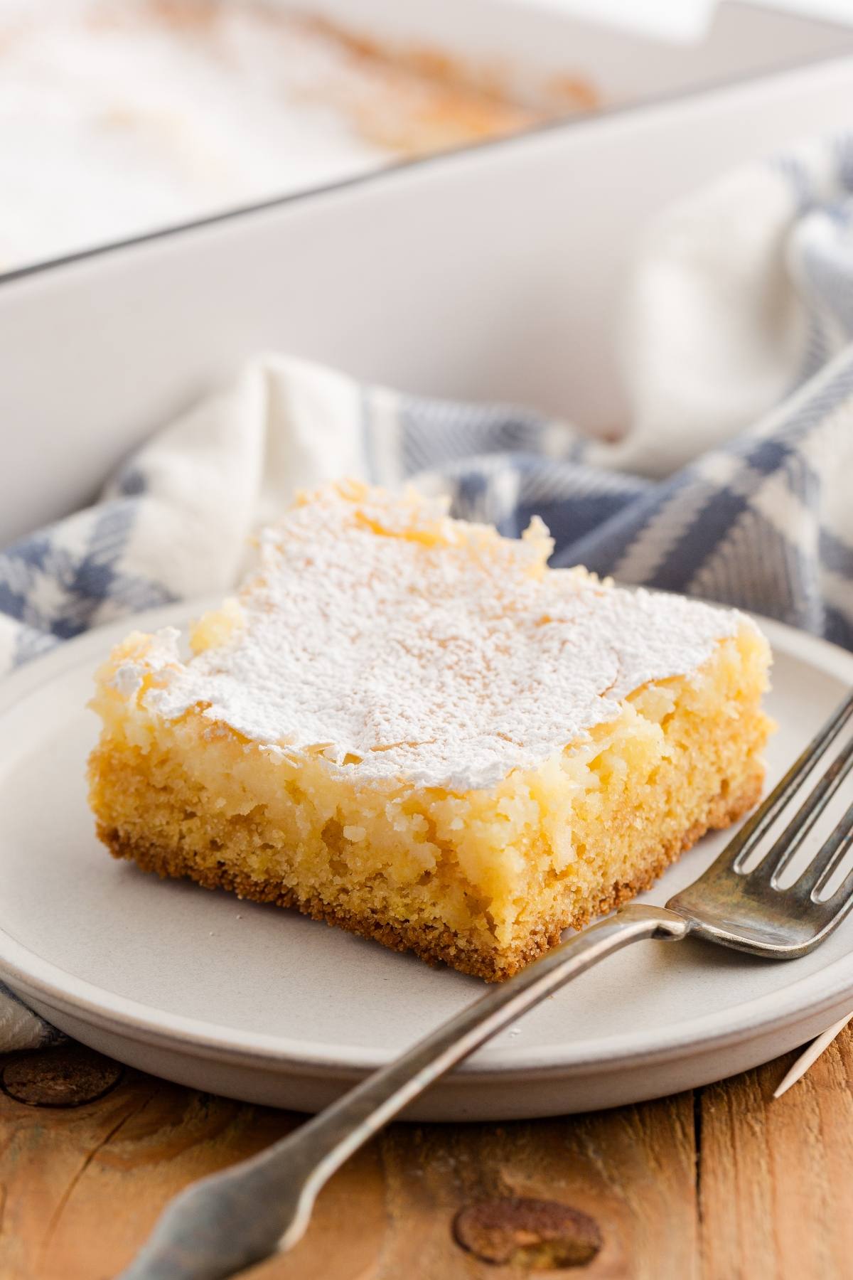 A square piece of gooey butter cake dusted with powdered sugar on a plate with a fork.