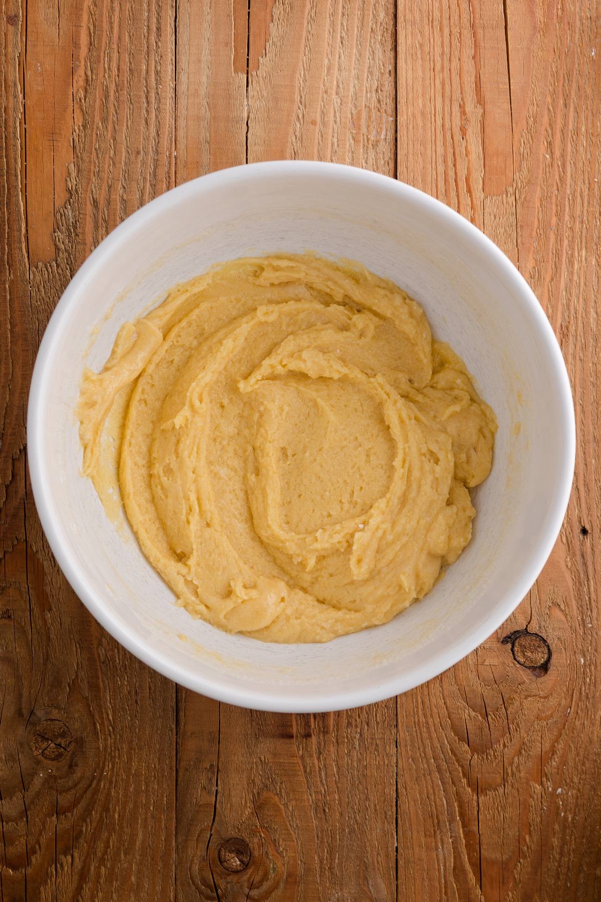A white bowl filled with creamy yellow cake batter on a wooden surface.