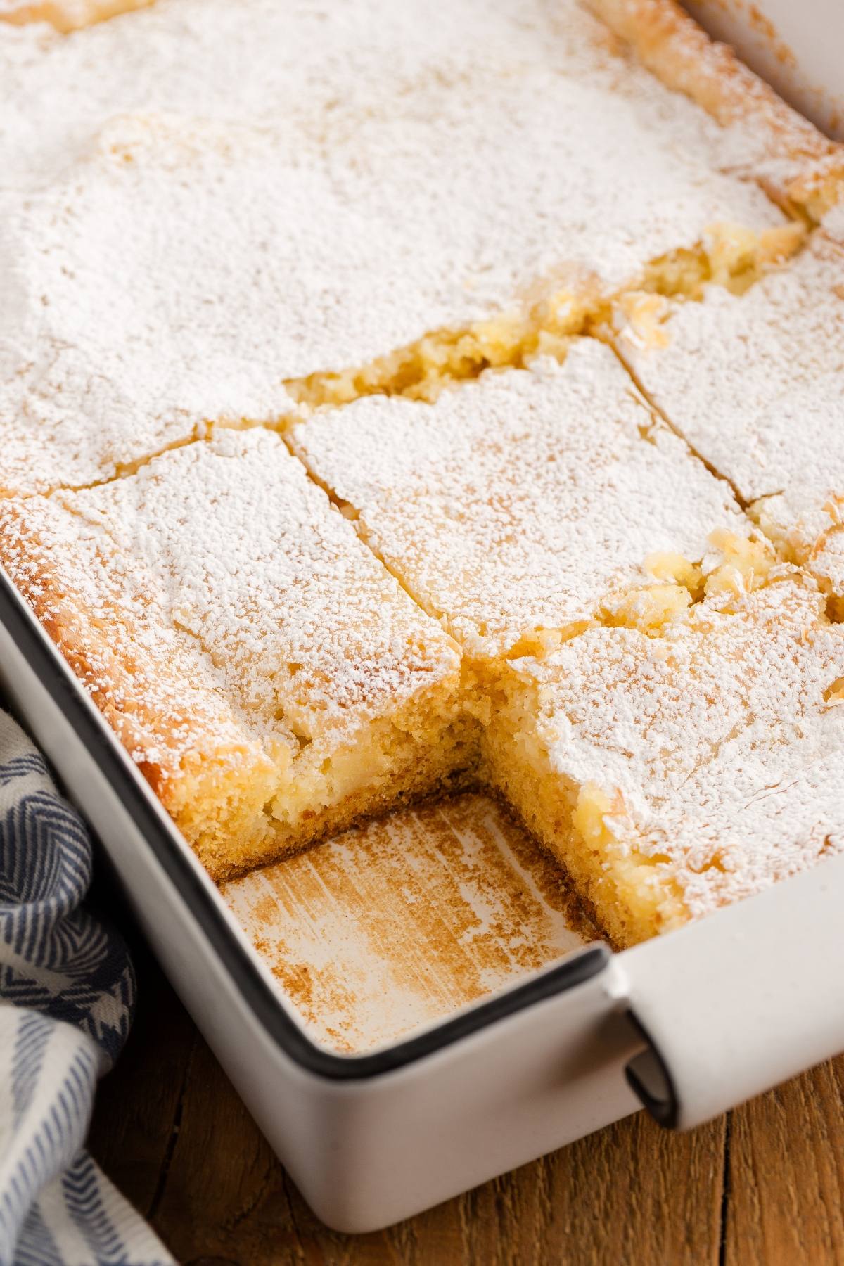 A pan of powdered sugar-dusted cake bars with some pieces cut and one missing.