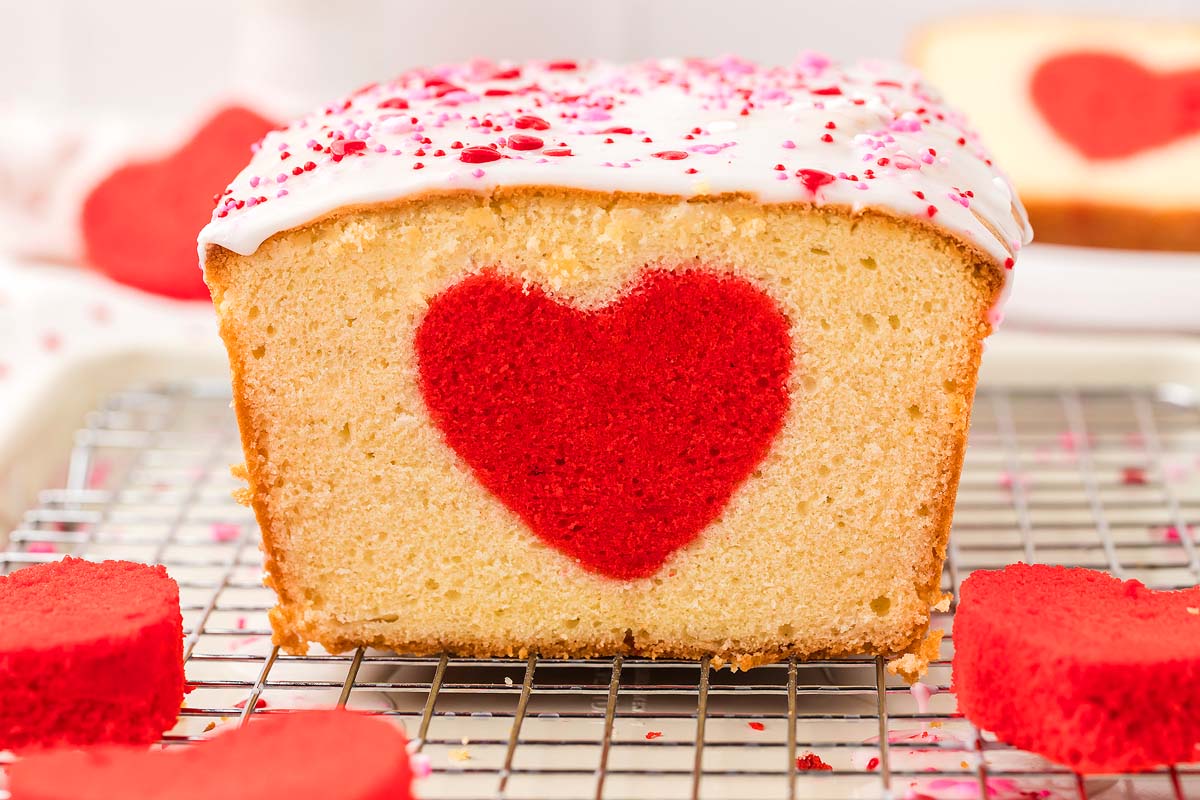 A hidden heart cake loaf featuring a red heart shape in the center, topped with white icing and pink sprinkles.
