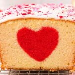 Loaf cake with a hidden heart cake design in the center, topped with white icing and pink sprinkles.