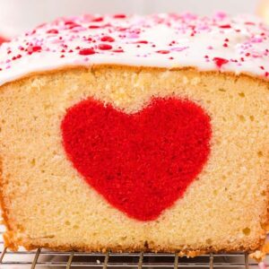 Loaf cake with a hidden heart cake design in the center, topped with white icing and pink sprinkles.