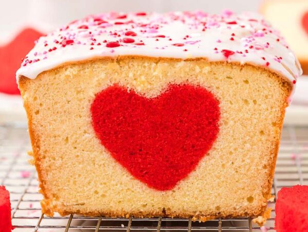 Loaf cake with a hidden heart cake design in the center, topped with white icing and pink sprinkles.
