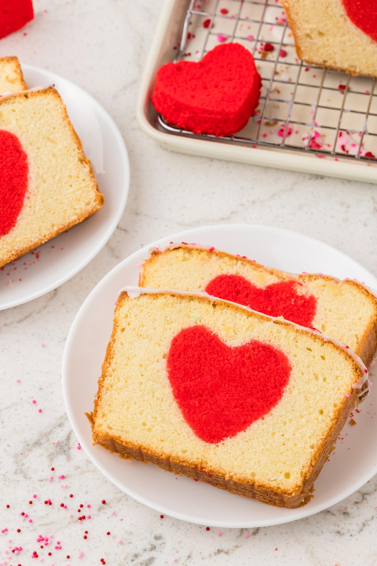 Two slices of hidden heart cake with red heart shapes in the center sit on a white plate.