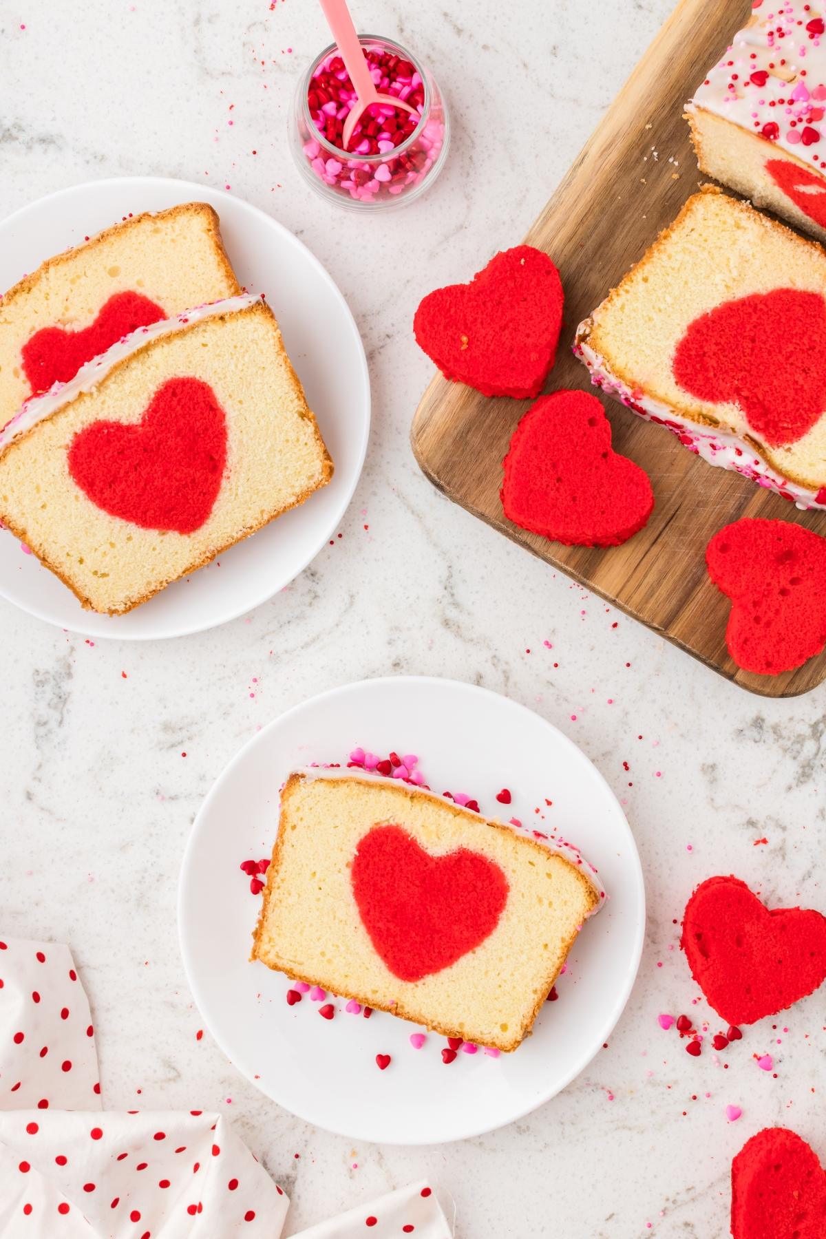 Slices of hidden heart cake with red heart shapes inside, served on white plates with heart-shaped sprinkles.