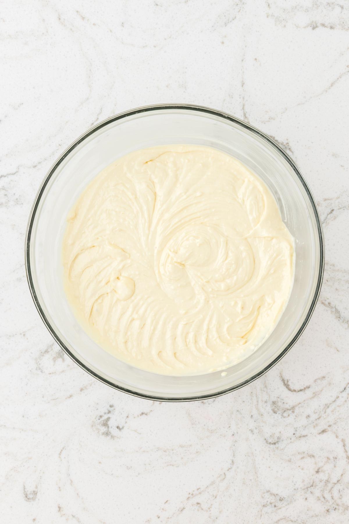 A glass bowl filled with creamy cake batter on a white marble countertop.